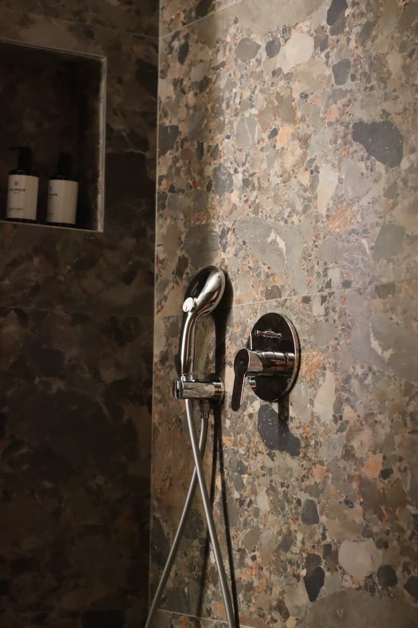A bathroom with a stone wall and a shower with a modern faucet.