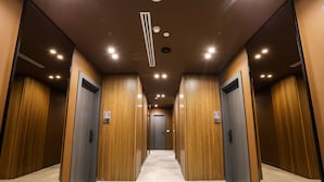 Ein moderner Hotelkorridor mit Holzvertäfelung an den Wänden, Fliesenboden und einer zentral gelegenen Tür am Ende.