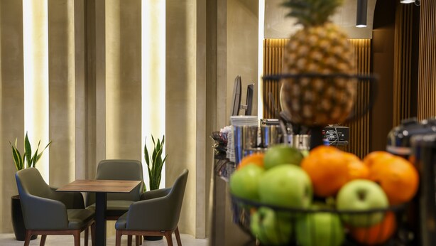 Ein moderner Essbereich mit einem Holztisch und Stühlen, einer Obstschale mit Äpfeln und Orangen, und einer Ananas auf einem Regal.
