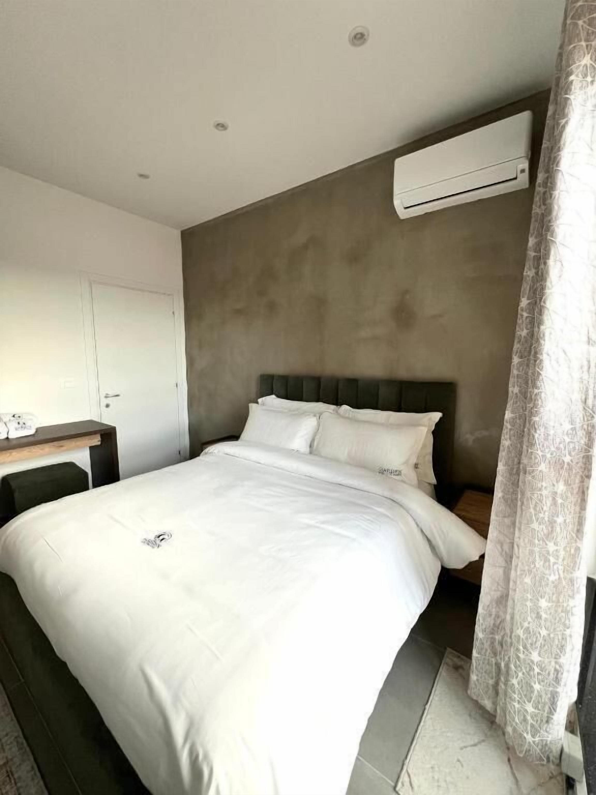Een moderne slaapkamer met een groot bed, een nachtkastje, een kledingkast en een airconditioner aan de muur.