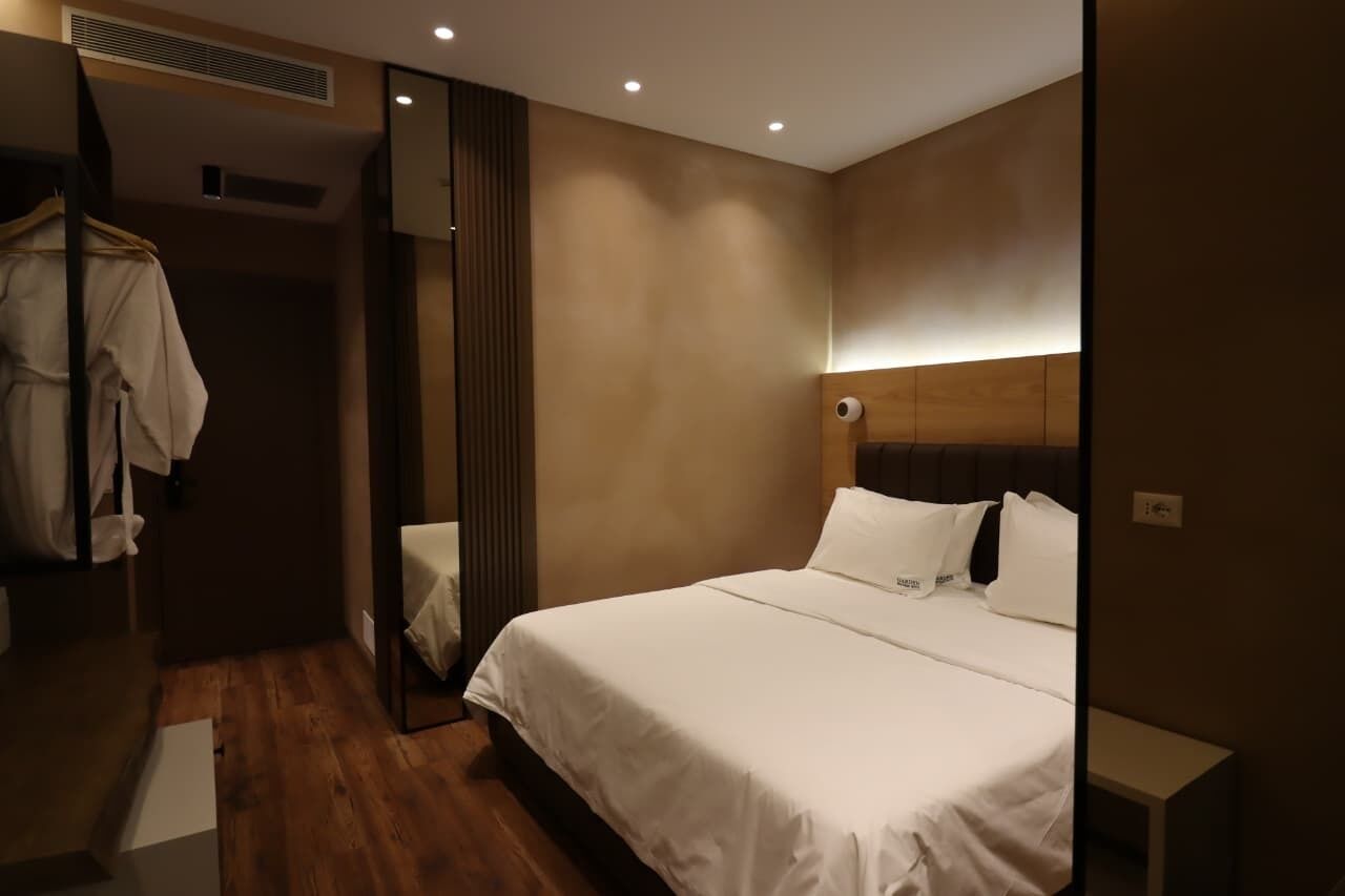 A hotel room with a large bed, a wardrobe, a mirror, and a bedside table.