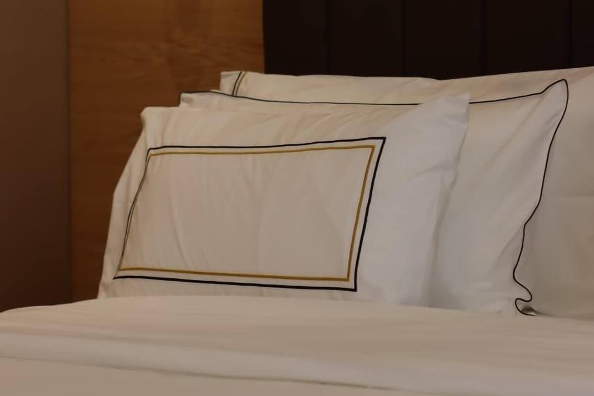 Een net opgemaakt bed met witte lakens en een donker hoofdbord.
