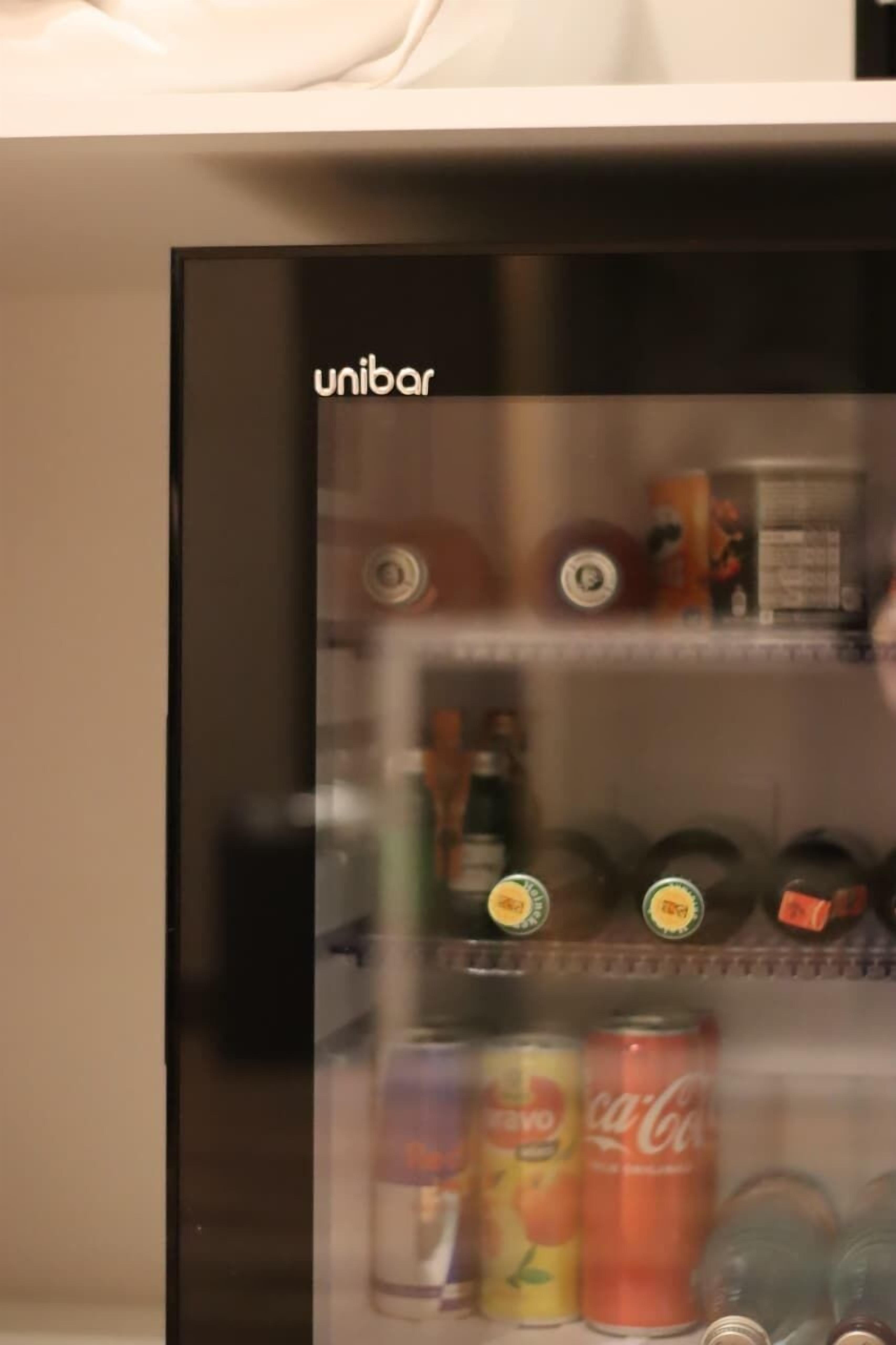 En minibar med ett urval av drycker, inklusive en burk Coca-Cola och en burk fruktjuice.