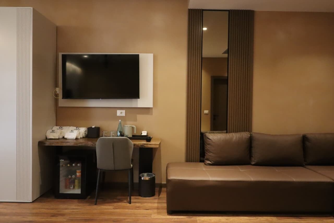 Une chambre d’hôtel moderne équipée d’un téléviseur à écran plat fixé au mur, d’un bureau avec une chaise, d’un canapé en cuir et d’un mini-bar.