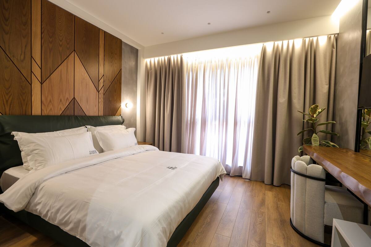 Een moderne hotelkamer met een groot bed, een wand van houten panelen en uitzicht op het omliggende landschap, verborgen achter gordijnen.