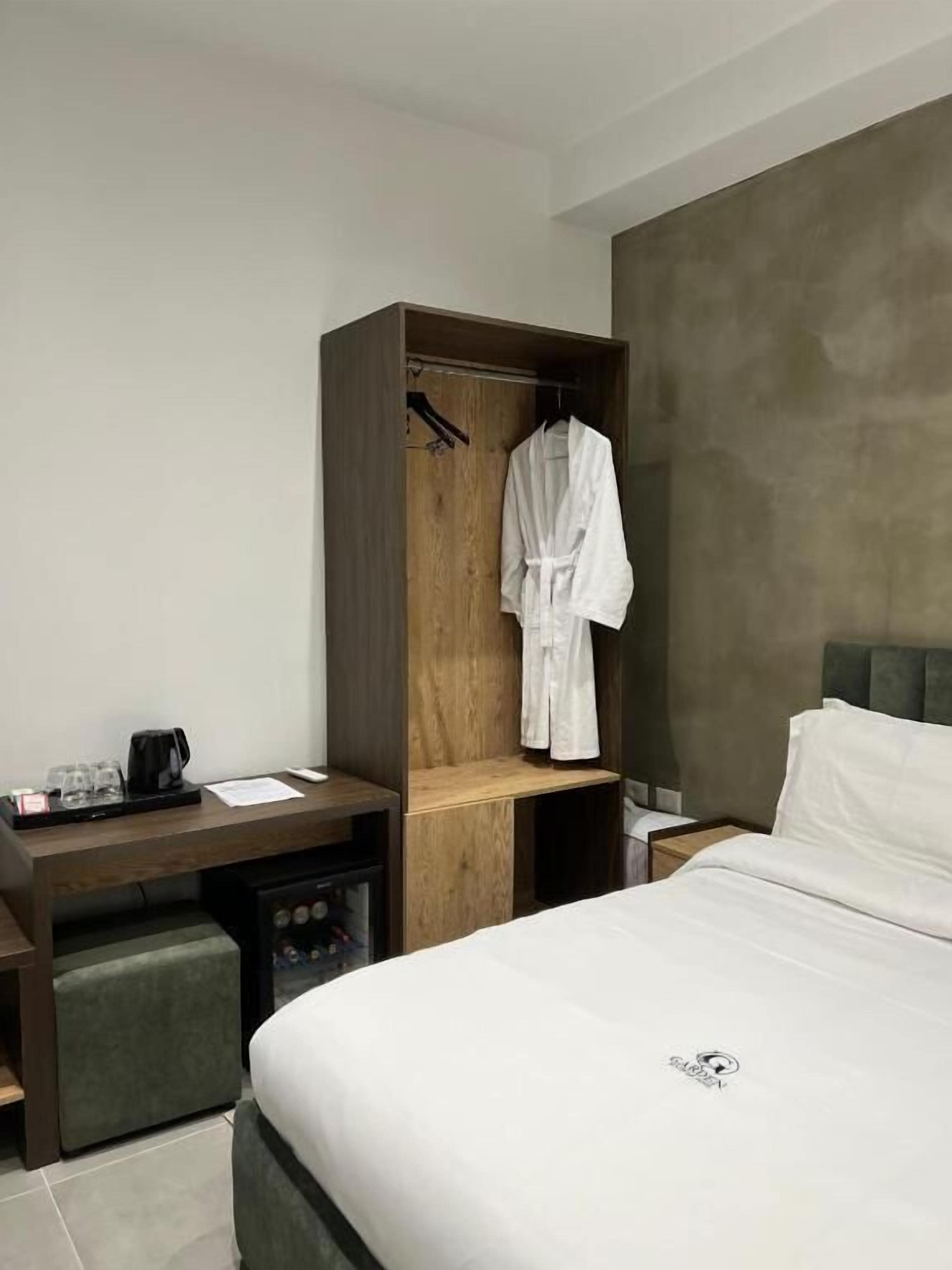 Una camera d'albergo con un letto, un armadio in legno, una scrivania con una macchina del caffè e un poggiapiedi verde.