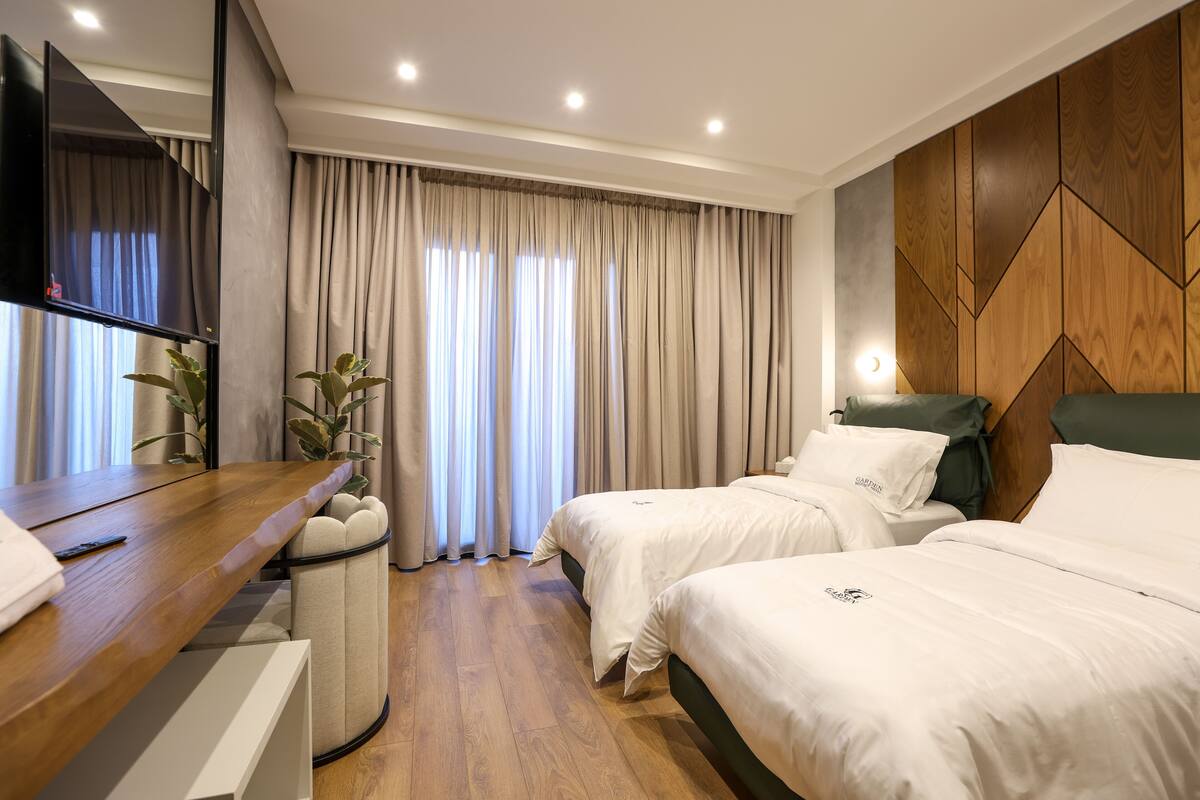 Een moderne hotelkamer met twee bedden, een bureau, een televisie en een groot raam met gordijnen.