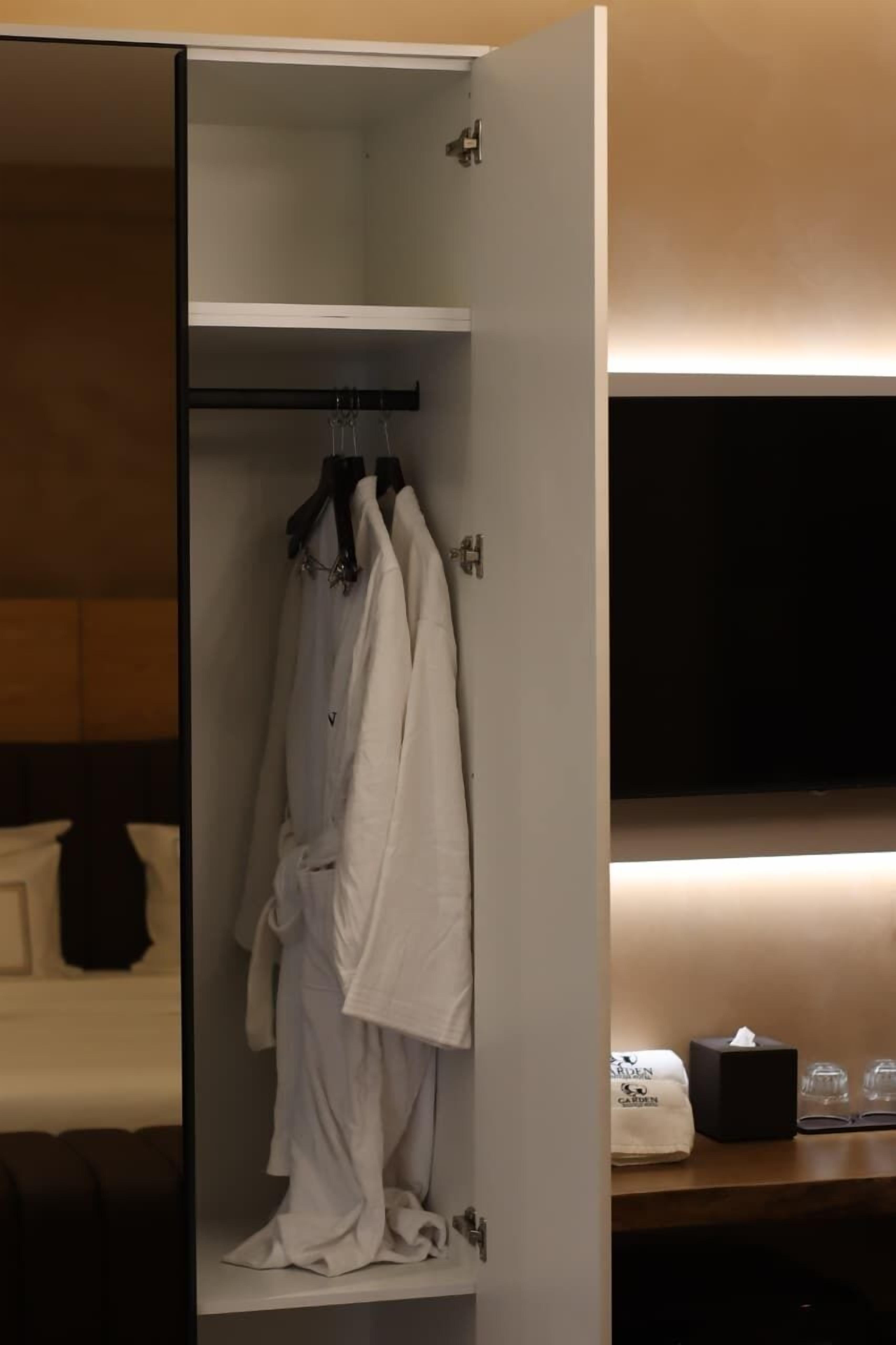 A hotel room with a walk-in closet containing a robe and a hanging garment.