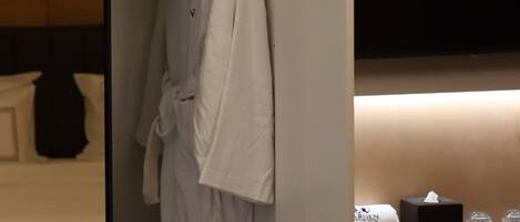 A hotel room with a walk-in closet containing a robe and a hanging garment.