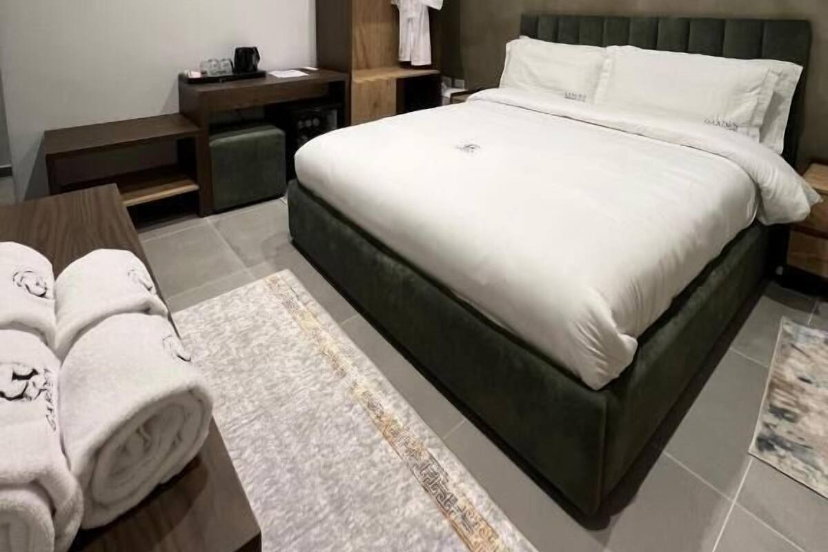 Een moderne slaapkamer met een groot bed, een houten garderobe, een bureau en een nachtkastje.