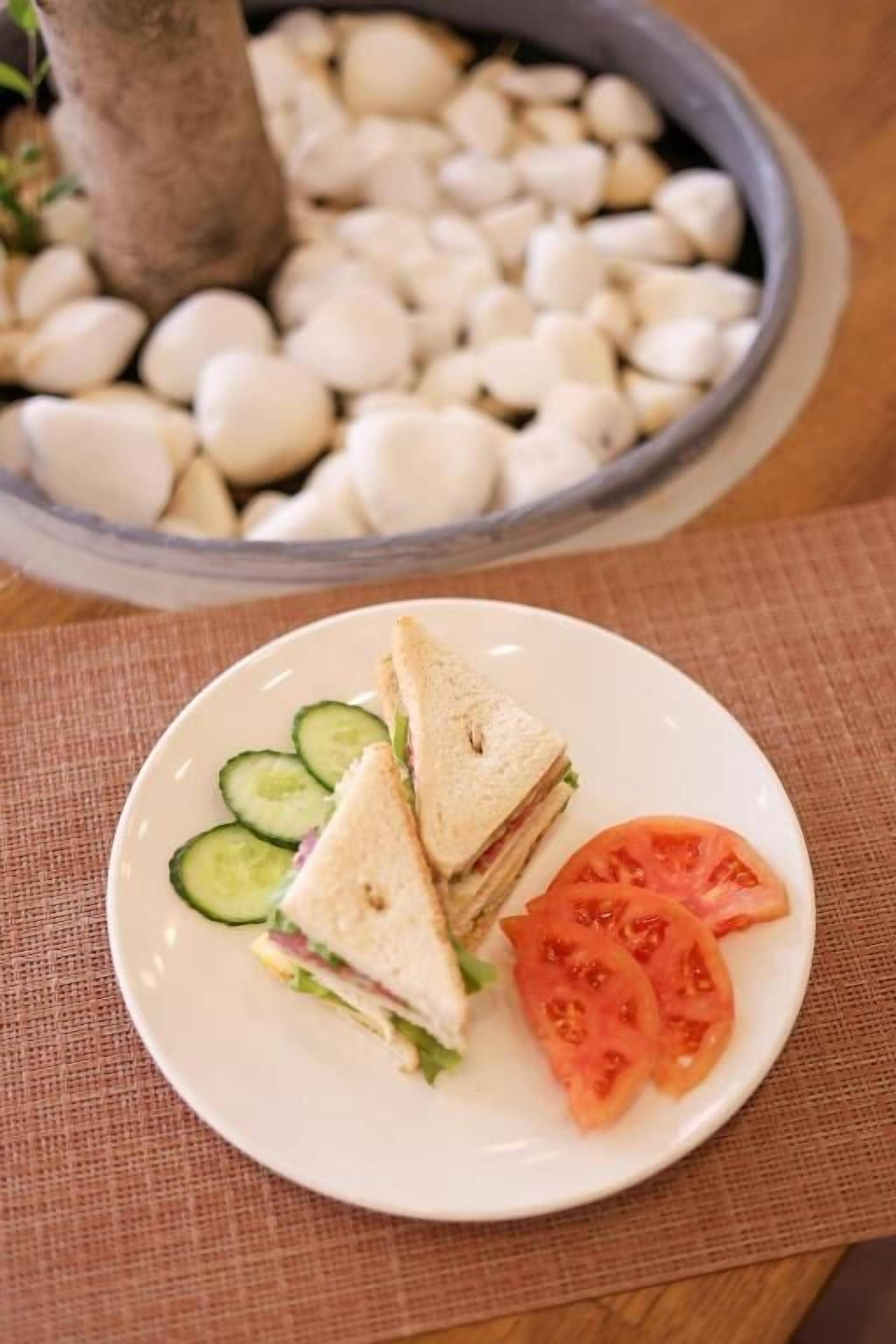 A plate with a sandwich, cucumber slices, and tomato slices on a table with a placemat.