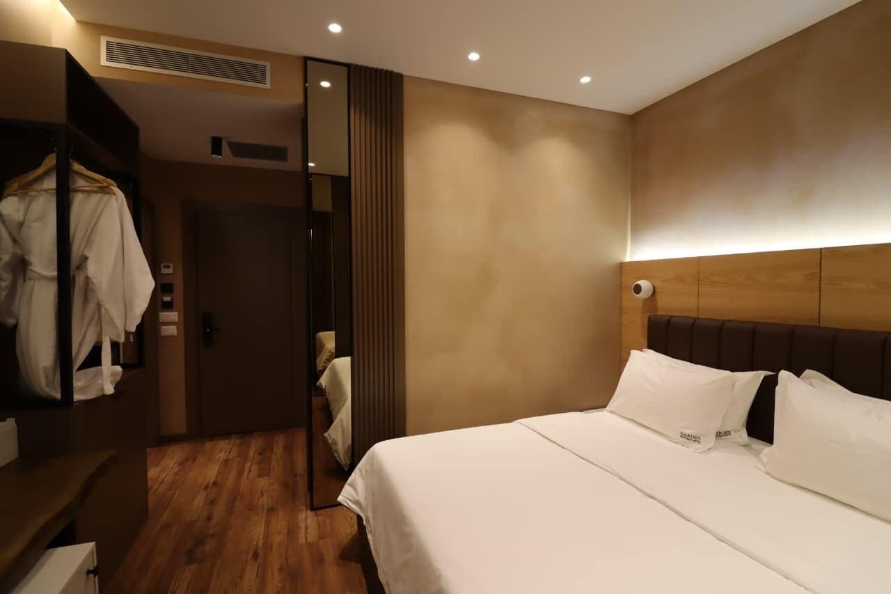 A hotel room with a wooden floor, a large bed with white linens, a wardrobe, and a mirror.
