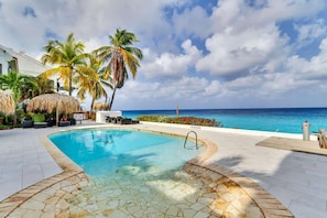 A swimming pool with a stone edge, surrounded by lounge chairs and palm trees, with a view of the ocean. - Belmar Oceanfront Apartments 12 located directly on the sea with diving facilities (Kralendijk)