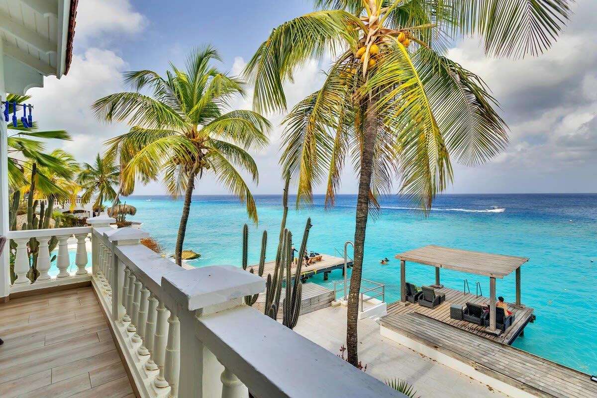 Een balkon met uitzicht op een turquoise oceaan en palmbomen.