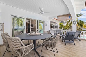 Un espace extérieur aménagé pour les repas, avec des chaises en osier et une table ronde, offrant une vue sur une piscine et des palmiers.