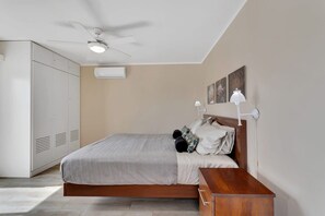 Une chambre à coucher comprenant un lit, une table de chevet, un ventilateur de plafond et une armoire.