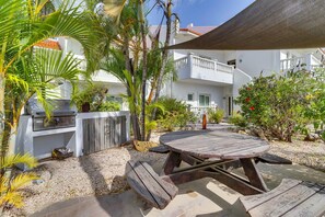 A patio area with a wooden table and grill, surrounded by palm trees and a white building with balconies. - Belmar Oceanfront Apartments 12 located directly on the sea with diving facilities (Kralendijk)