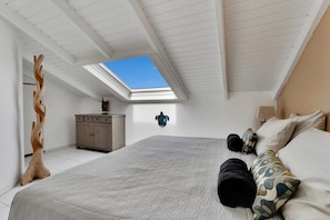 Ein Schlafzimmer mit Oberlicht, einem Bett mit gemusterten Textilien, einer Holz-Baumskulptur und einem Schrank.