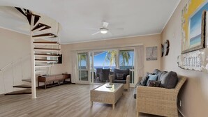 Ein geräumiges Wohnzimmer mit Wendeltreppe, einem großen Fenster mit Meerblick und einem Korbsessel.