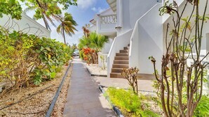 Ein Weg, gesäumt von weißen Gebäuden, einer Palme und einer Treppe, die zu einem Balkon führt.