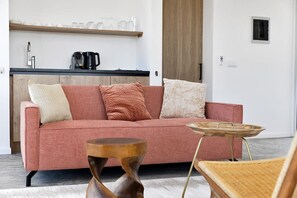 Una sala de estar moderna con un sofá rosa, una mesa de centro de madera y una zona de cocina al fondo.