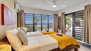 A hotel room with two beds, a ceiling fan, and a large window with curtains. - Villa Heros Sabadeco (Kralendijk)