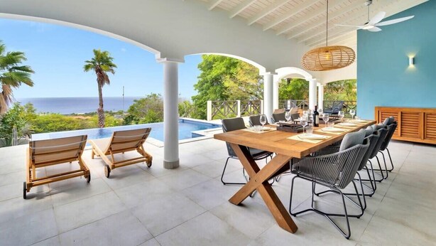 A covered outdoor dining area with a pool, wooden chairs, and a table set for dining. - Villa Heros Sabadeco (Kralendijk)