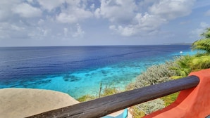 A coastal view with clear turquoise waters, a sandy beach, and a wooden railing. - Villa Kokopelli with stunning sea views and a refreshing private pool (Kralendijk)