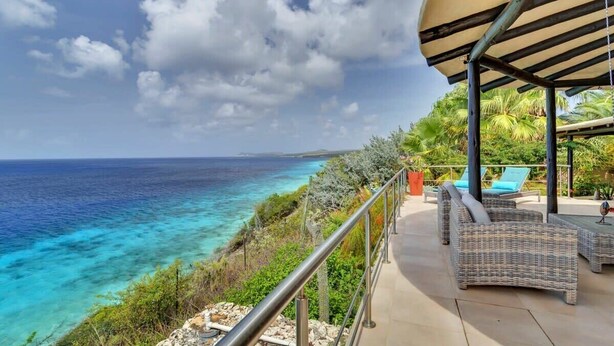 A balcony with wicker furniture overlooking a turquoise sea and a clear sky. - Villa Kokopelli with stunning sea views and a refreshing private pool (Kralendijk)