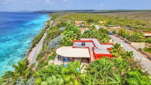 A coastal property with a large house featuring a curved roof, a swimming pool, and lush greenery. - Villa Kokopelli with stunning sea views and a refreshing private pool (Kralendijk)