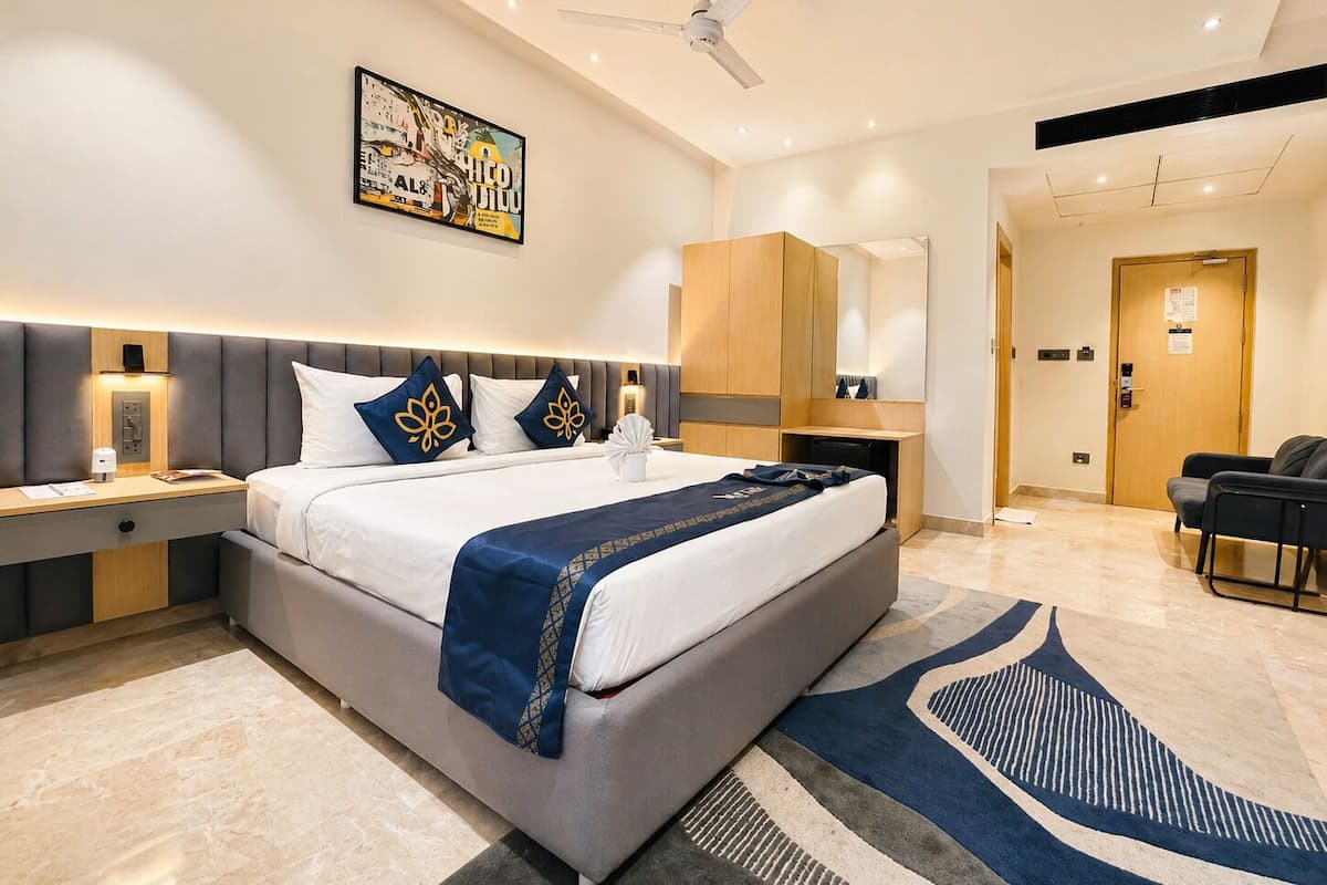 A modern hotel room with a large bed, bedside tables, a desk, a chair, a ceiling fan, and a large mirror.