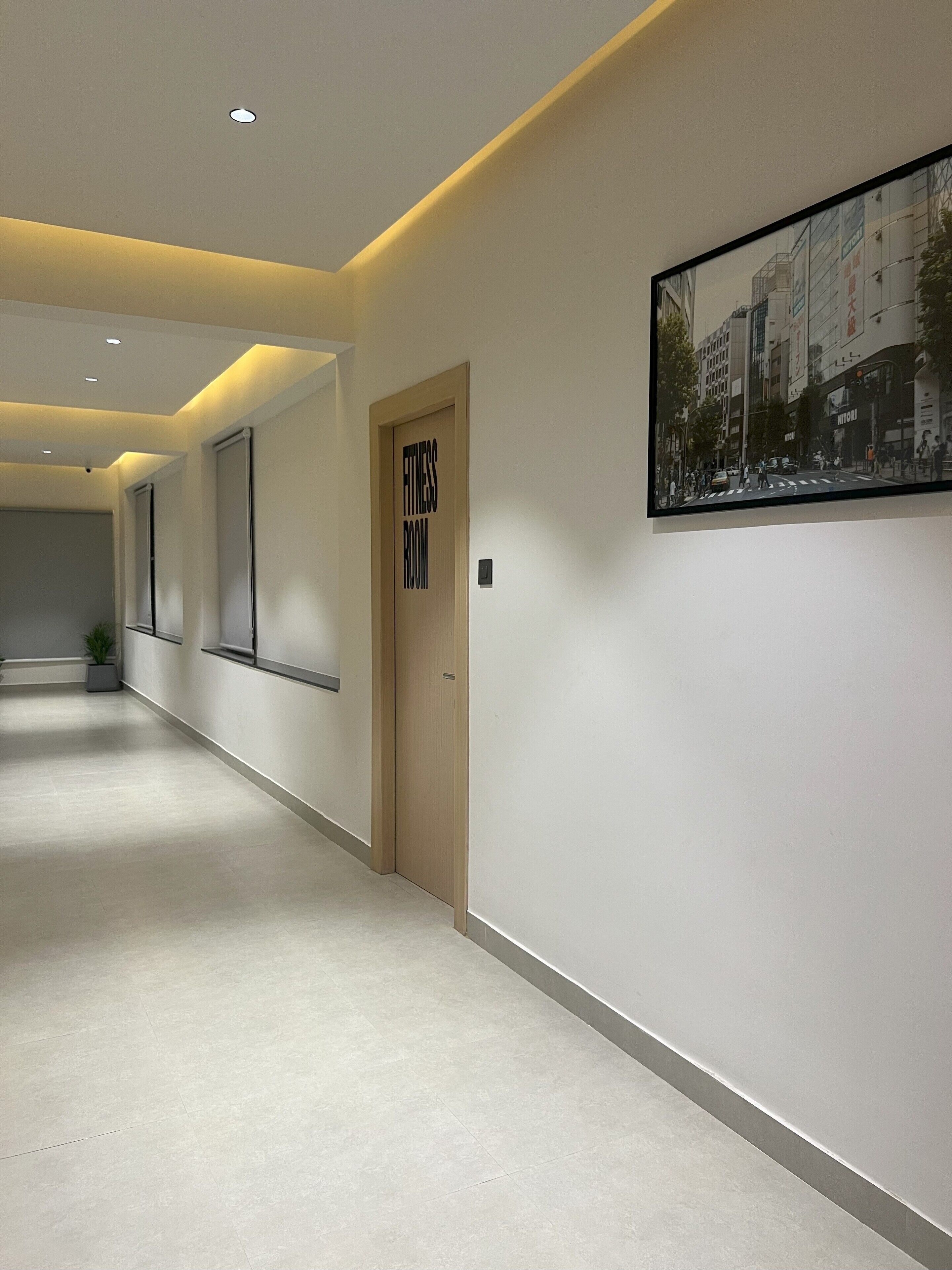 A modern hallway with recessed lighting, a fitness room sign, and a framed cityscape photo on the wall.