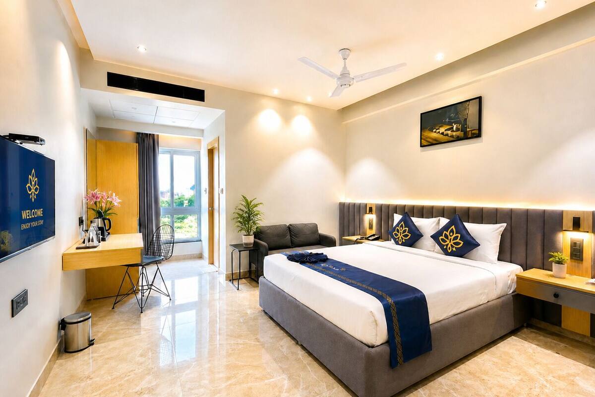 A modern hotel room with a large bed, a desk, a chair, a TV, and a ceiling fan.