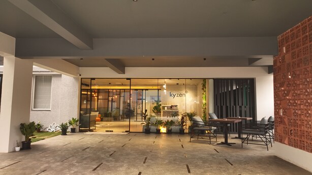 A modern cafe with a glass entrance, outdoor seating, and a brick accent wall. - Hotel Kyzen - Hitec city, Hyderabad (Hyderabad)