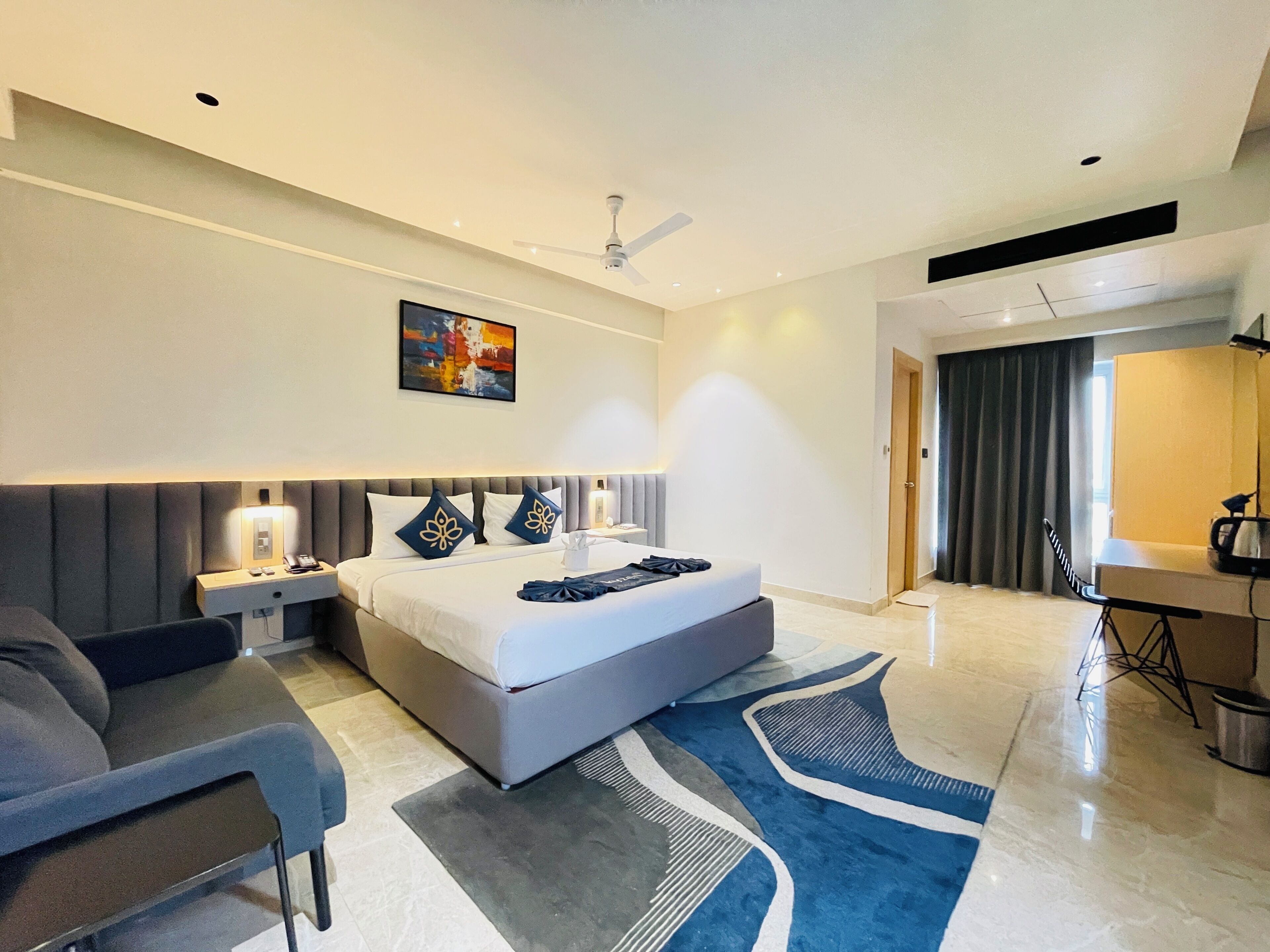 A modern hotel room with a large bed, a desk, a chair, and a ceiling fan.