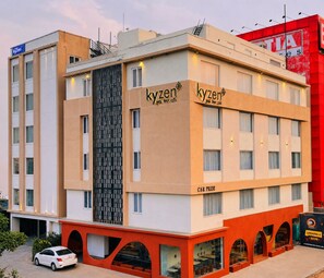 Un hotel con diseño moderno, destacando un letrero grande de 'kyzen', múltiples ventanales y una paleta de colores rojo y beige.