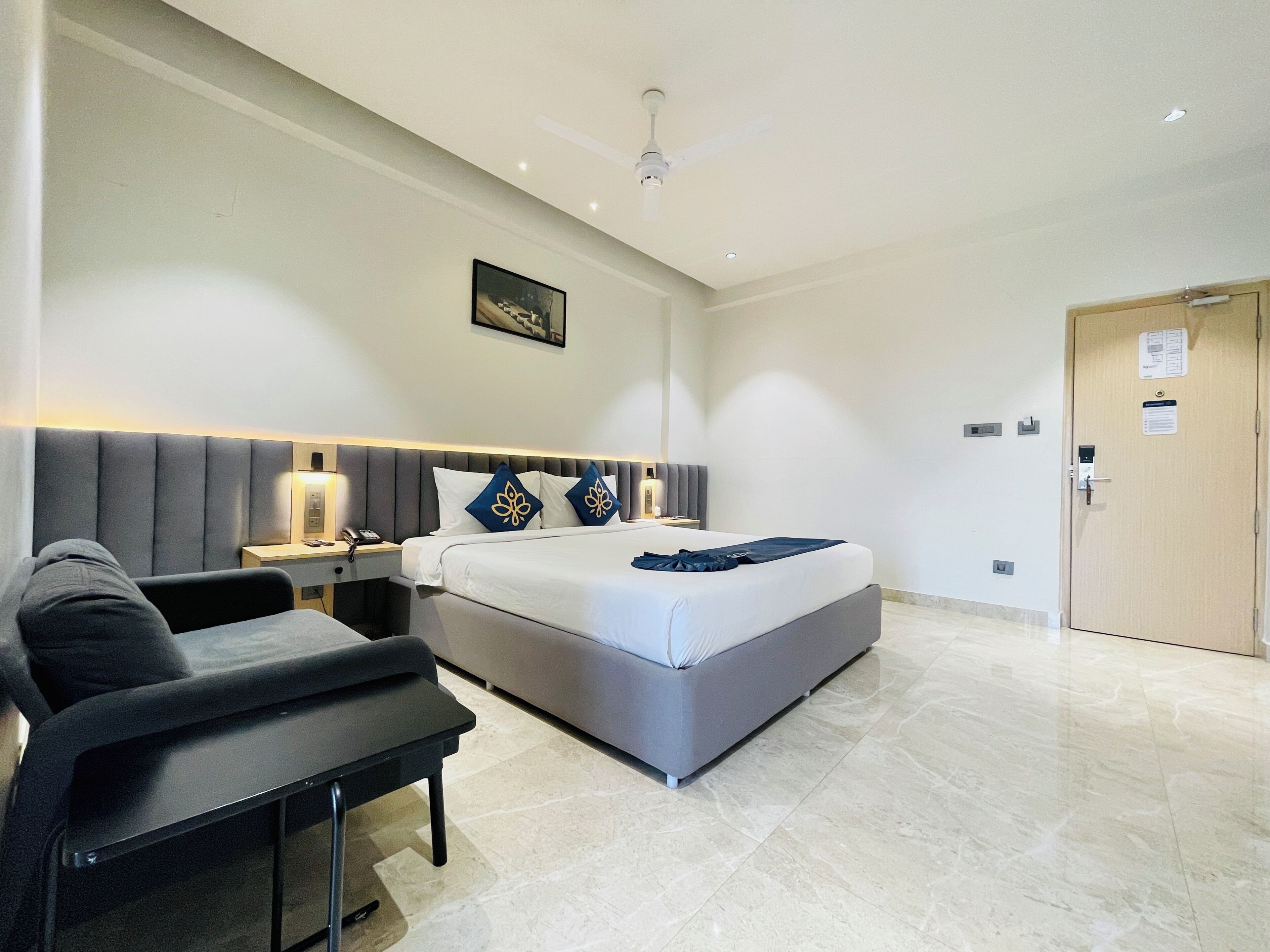 A modern hotel room with a large bed, a desk, a chair, and a door.