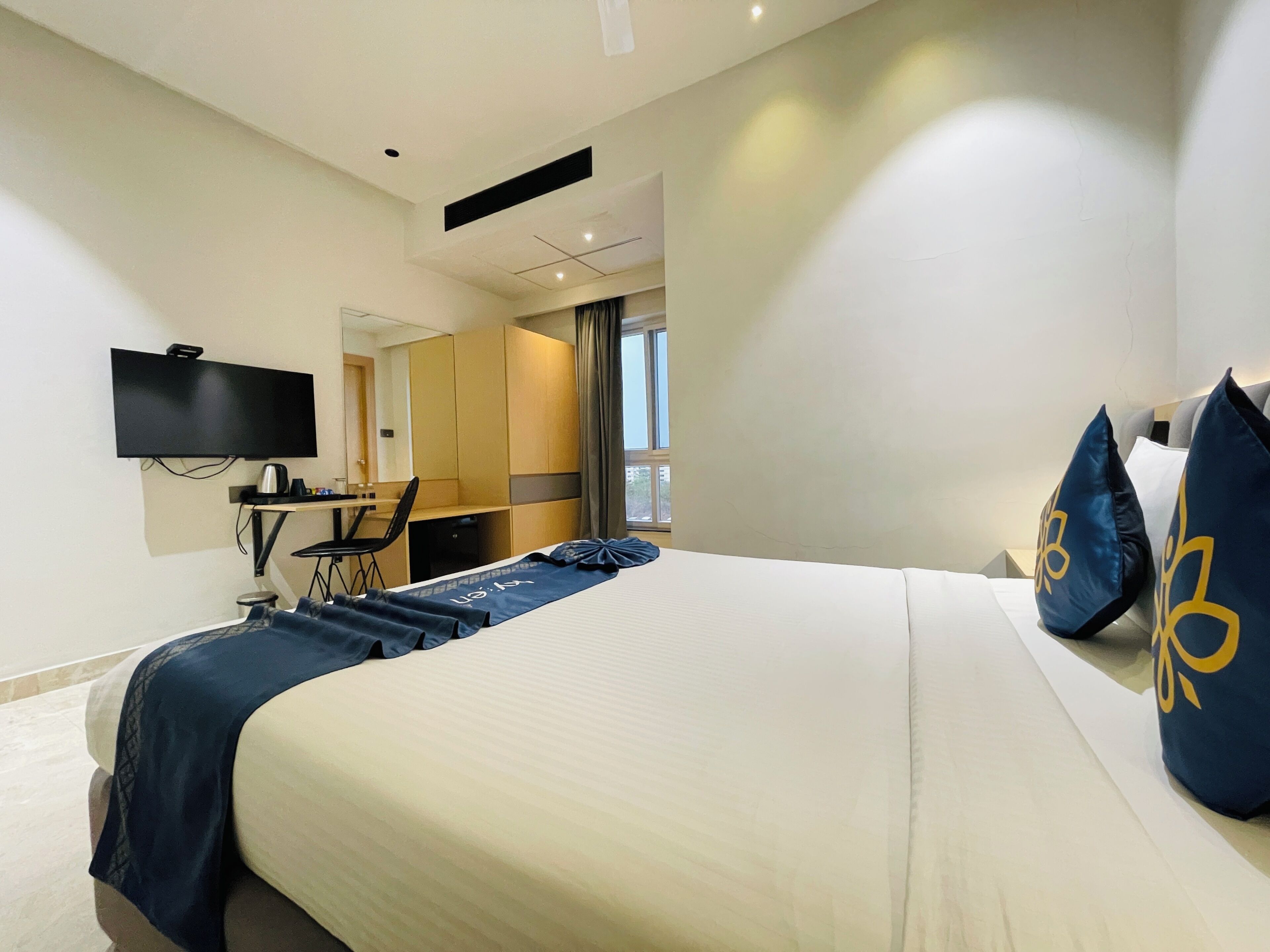A hotel room with a bed, a desk, a chair, a television, and a window.