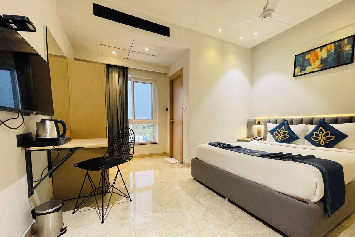 A modern hotel room with a bed, a desk with a chair, a coffee maker, and a trash bin.