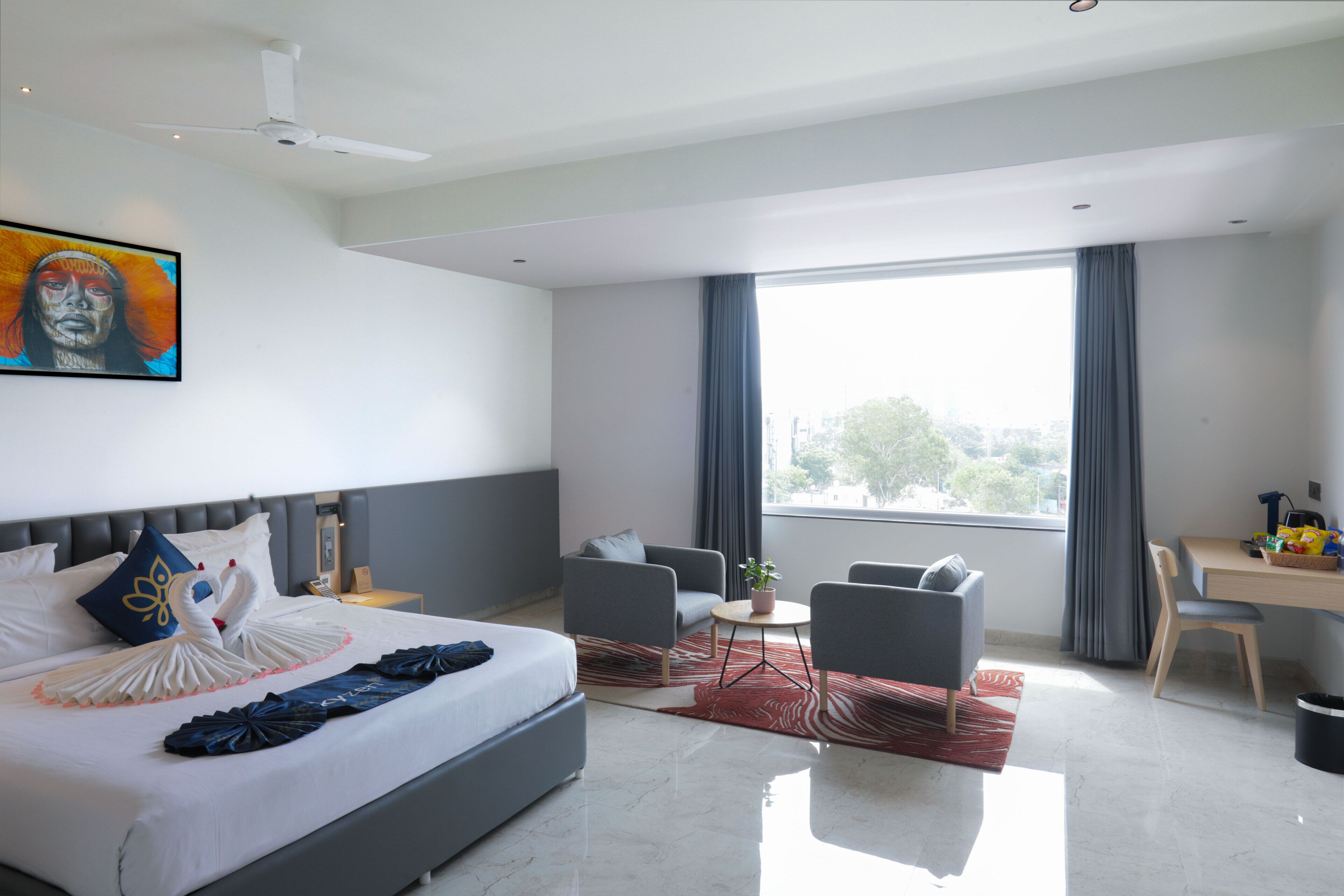 A modern hotel room with a large bed, a desk, a chair, and a view of the outdoors.