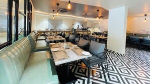 A restaurant with a modern interior, featuring a long counter with seating, pendant lighting, and a patterned floor. - Hotel Kyzen - Hitec city, Hyderabad (Hyderabad)
