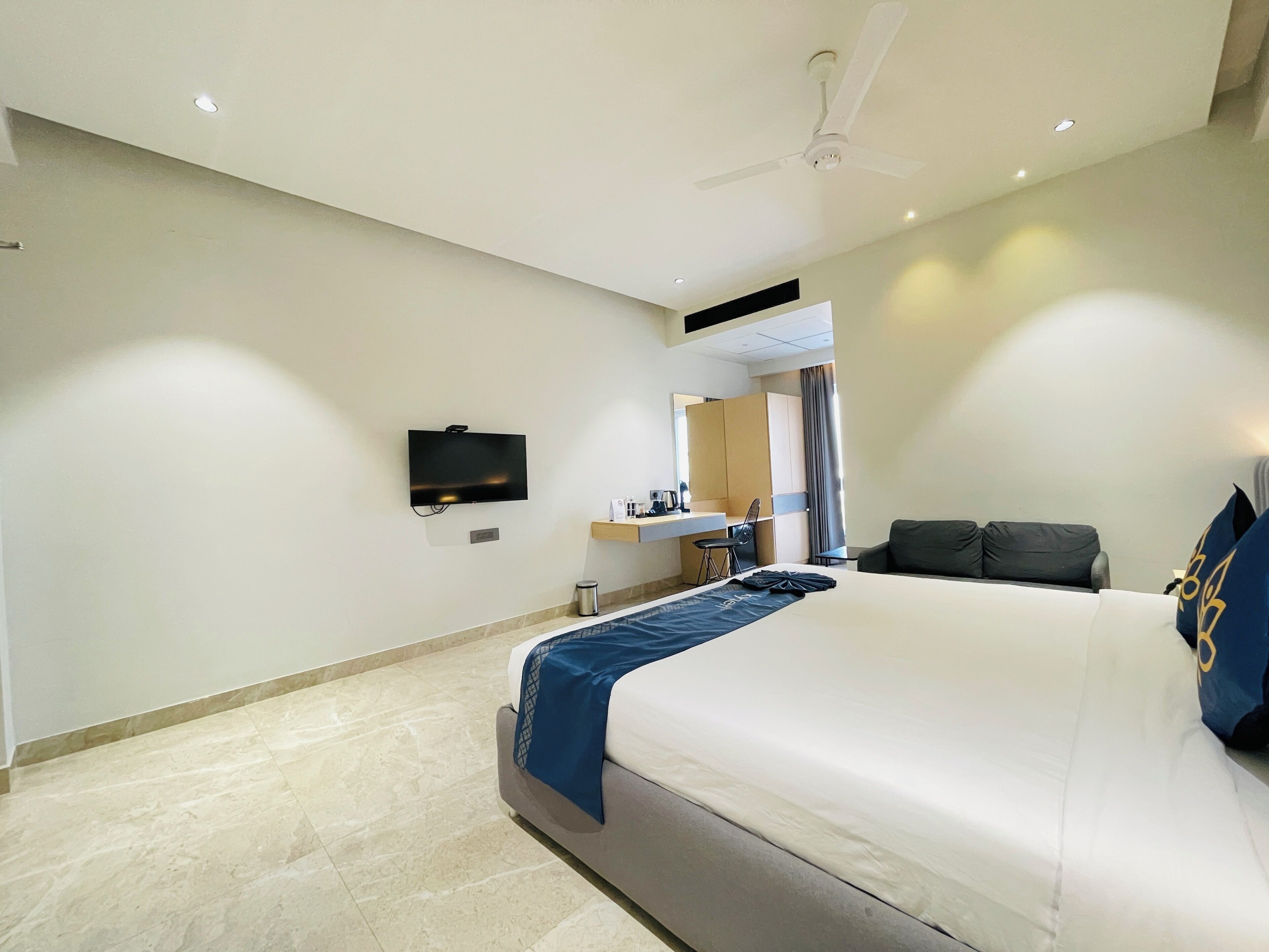 A hotel room with a bed, a desk, a chair, a television, and a ceiling fan.