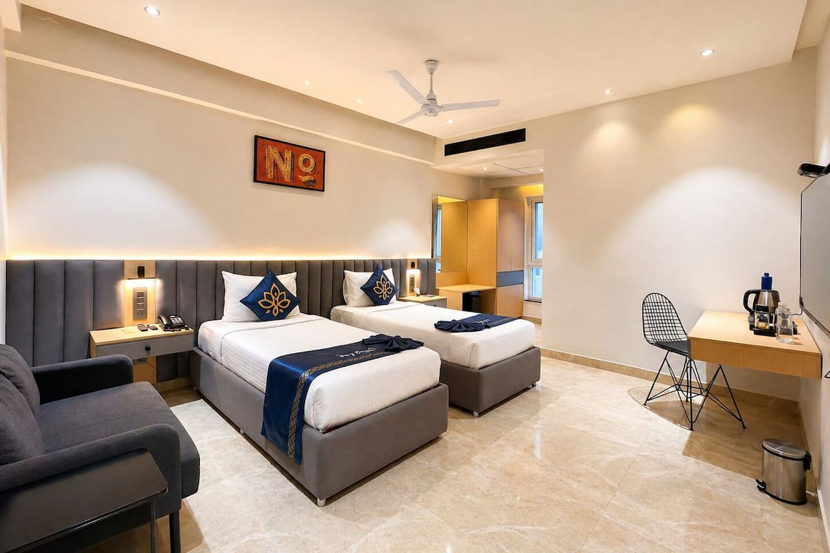 A modern hotel room with two beds, a desk, a chair, a trash bin, and a ceiling fan.