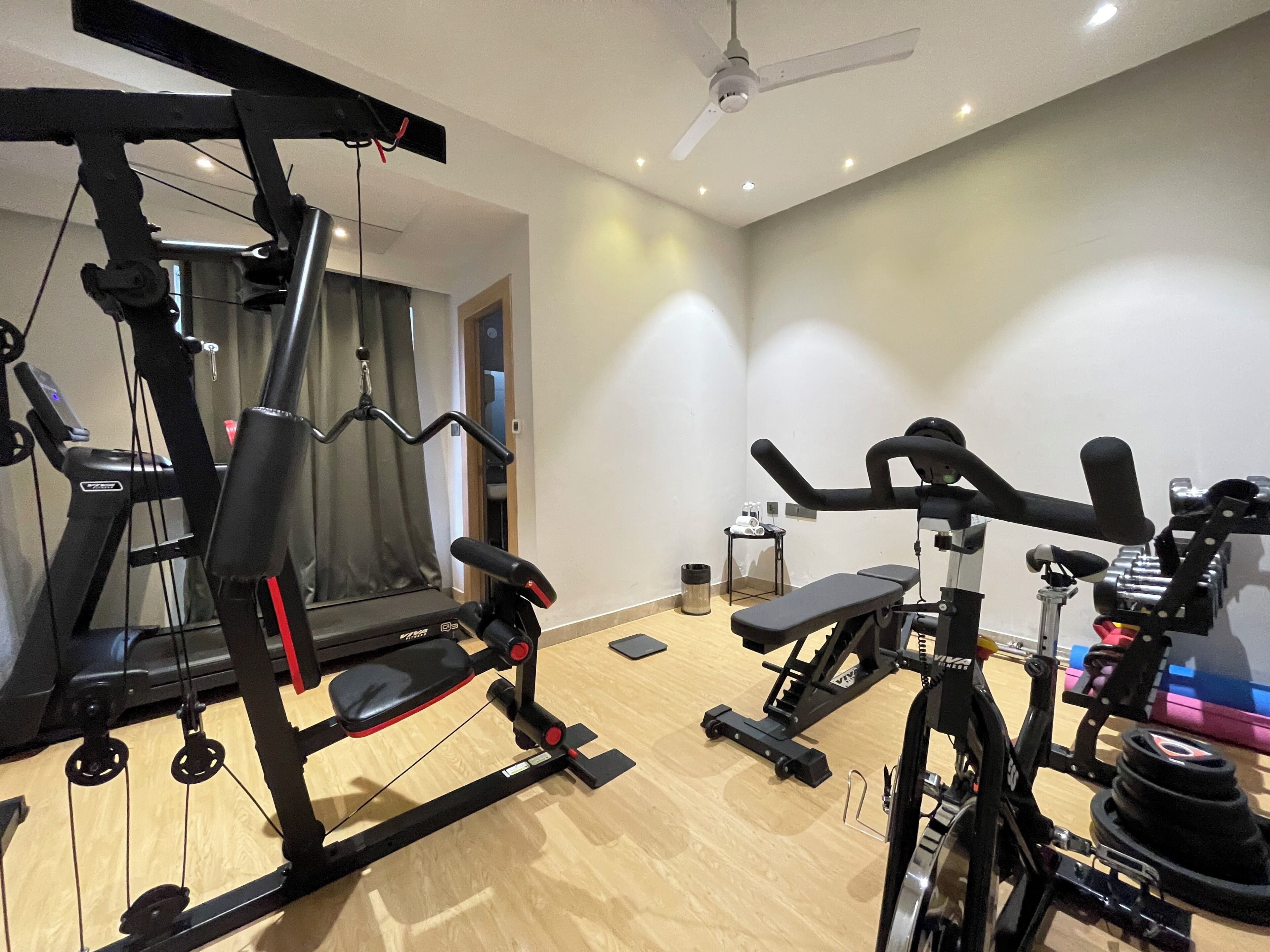 Een sportschool met trainingsapparatuur, een plafondventilator en een klein tafeltje met een waterfles.
