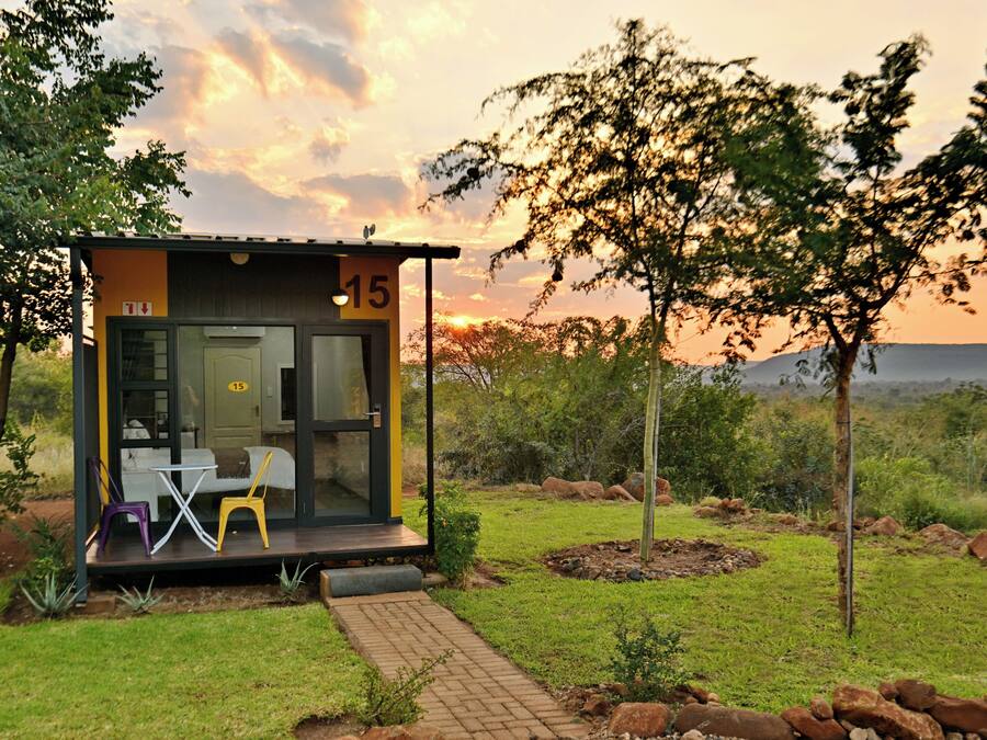 Una estructura moderna, envuelta en vidrio, con un letrero con el número 15, mesas al aire libre y un paisaje natural al fondo.