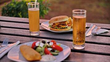 A meal with a burger, salad, and a fried item on a wooden table with beer glasses.