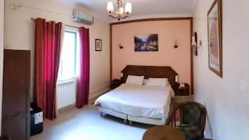 Un dormitorio con cama, una silla, radiador, ventana con cortinas y un cuadro en la pared.