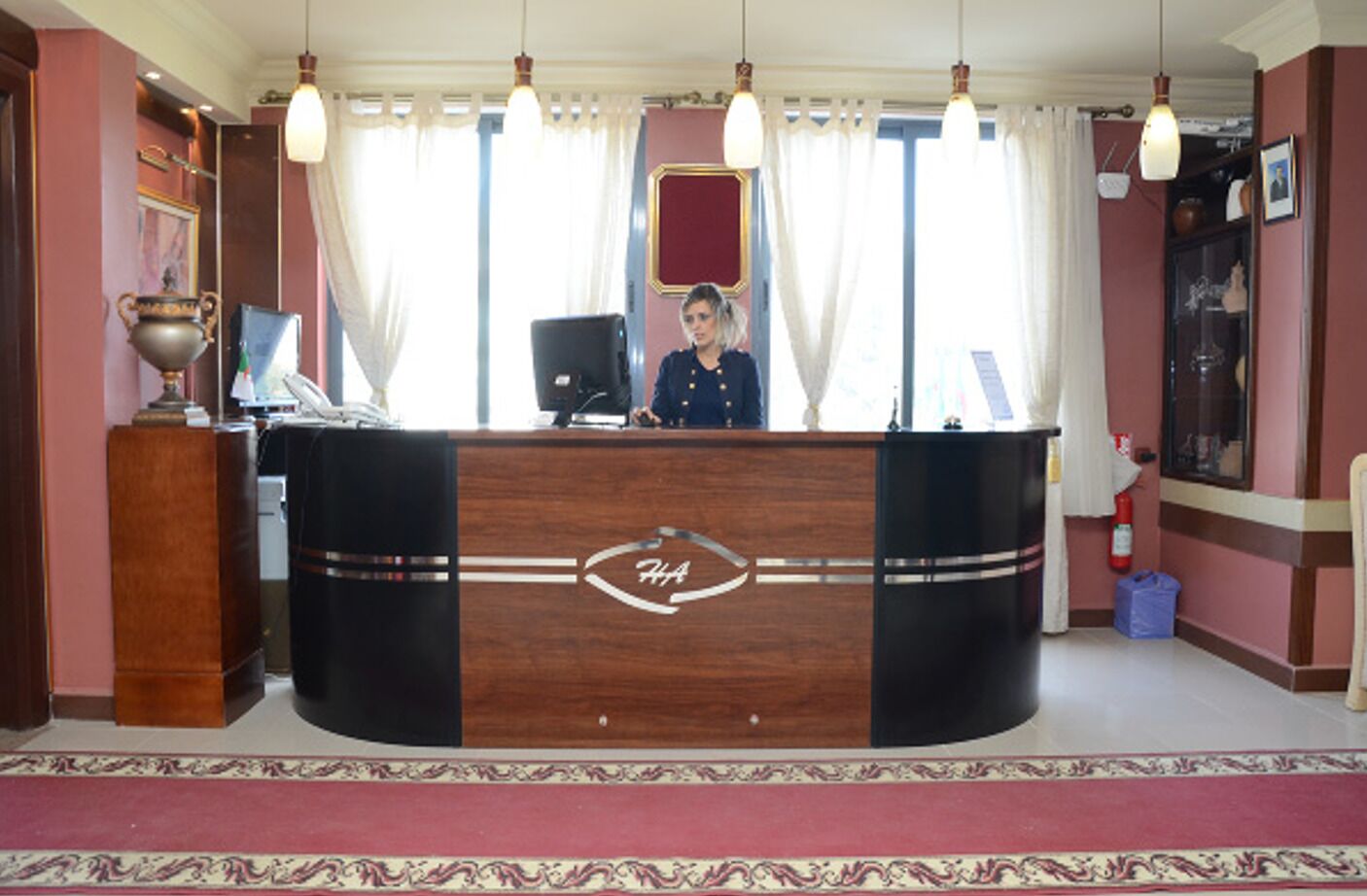 A reception desk with a logo, a receptionist, and a decorative vase.