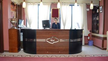 A reception desk with a logo, a receptionist, and a decorative vase.