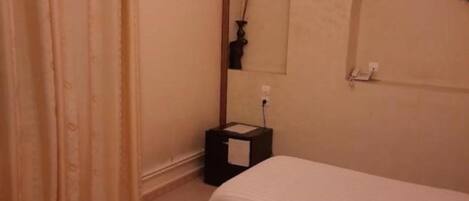 A hotel room with two beds, beige curtains, a wall clock, and a small table with a lamp.